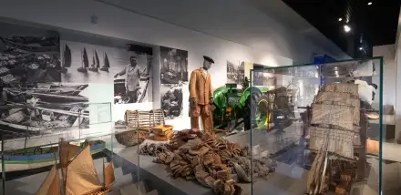 Vue de l'xposition une histoire de Bretagne avec des maquettes de bateaux, des photographies et des vêtements de travail.