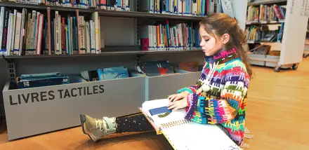 Une enfant lit un livre en tactile en braille à l'espace Chez Les Enfants de la bibliothèque.