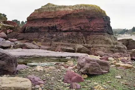 Photographie de l'Ande de Bréhec en Côtes d'armor. Une roche rouge se détache d'une plage de galet.