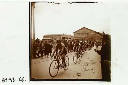 Une image stéréoscopique du Tour de France à Rennes en 1934. Des coureurs à vélo se succèdent à la file indienne devant une foule qui les applaudit.