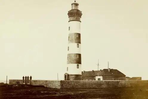 Photographie montrant l'ensemble du site du phare du Créac'h (enceinte faite d'un mur de pierres avec double portail, phare et bâtiments à l'intérieur de l'enceinte). Deux personnages sur la gauche (peu visibles).