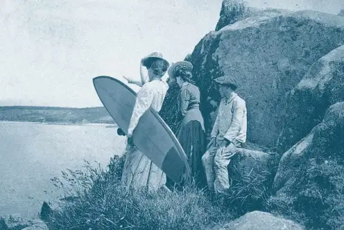 Deux femmes, dont l'une tient une planche de surf, et un enfant regardent la mer