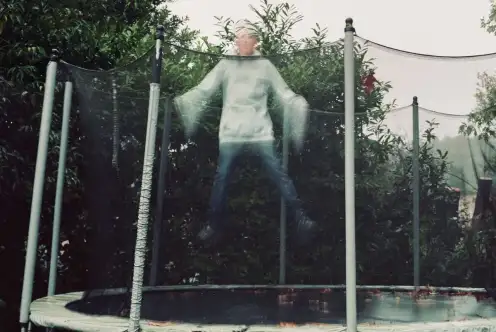 Sur un trampoline, dans un jardin vert, un enfant saute, flou, pris dans le mouvement.