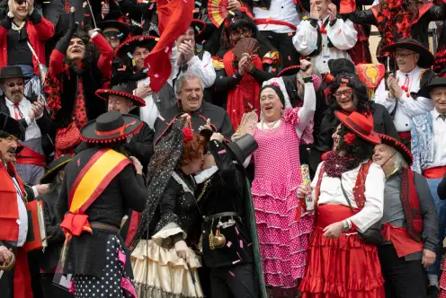 Une foule prise en photo de près, habillés de blanc, rouge et noir; semble fêter le baiser de deux personnes. L'ambiance est à la liesse.