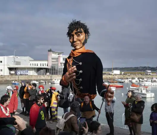 Sur cette photographie prise à Douarnenez, un groupe de personnes sur le port de Douarnenez admire une grande effigie représentant un corsaire géant