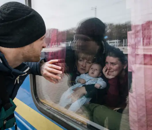 Photographie couleur d'un homme sur le quai d'une gare. Il a la main posé sur la vitre d'un train pour saluer une famille avec un bébé à l'intérieur du wagon.