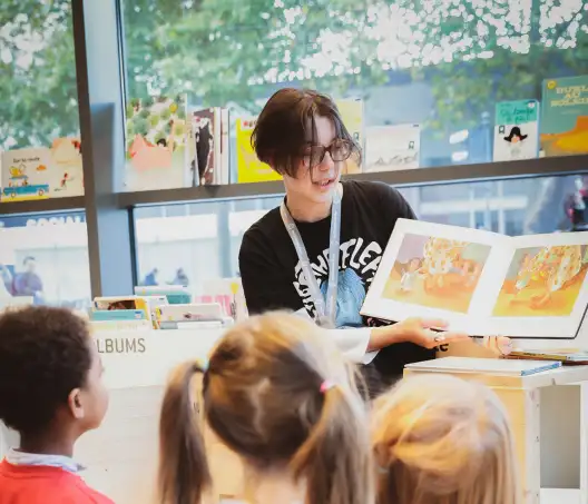 Julien Mignot, CC-BY-SA. Une personne lit un album pour enfants au rez-de-chaussée de la Bibliothèque des Champs Libres devant un public de 3 à 6 ans.