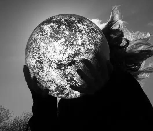 photographie en noir blanc d'une personne tenant un globe de verre dans ses mains. La photographie est prise en contrejour.