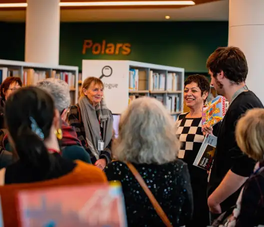 dans la Bibliothèque, une autrice anime une rencontre avec des visiteurs dans les rayons.