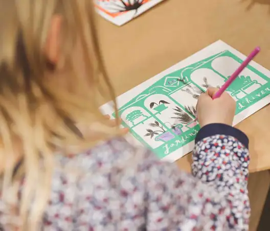 Photographie d'une  jeune enfant blonde en train de colorier une illustration sur laquelle il est écrit Jardins d'hiver