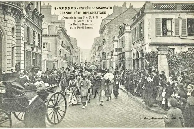 Photographie en noir d'un défilé, rue du Maréchal-Joffre à Rennes. Au premier plan, dans une calèche, la reine de Madagascar Ranavalo. Suit un défilé de personnes costumées portant le nom de "Péril Jaune". Parmi les spectateurs, des femmes portent la polka (coiffe).