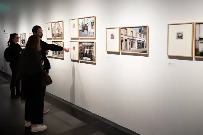 Une photographie de l'exposition photographique. Trois personnes regardent les photos encadrées.