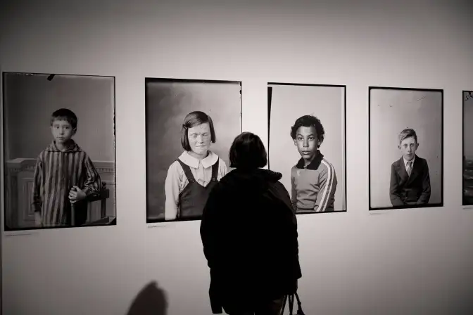 Une photographie en noir et blanc d'une personne, de dos, regardant quatre photographies d'enfants.