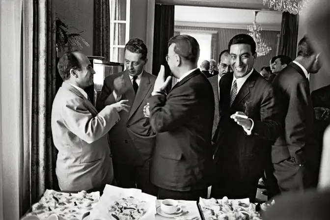 Un groupe d'homme en costume discutent et sourient en intérieur