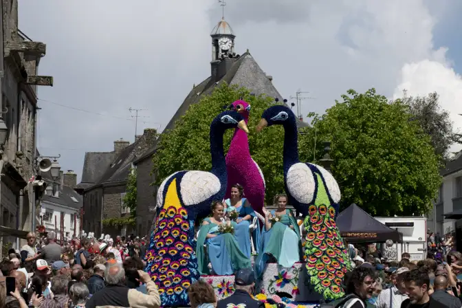 Un char décoré avec trois paons sur lequel sont installées les reines du carnaval