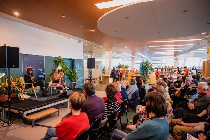 Dans la Bibliothèque a été installé une scène sur laquelle parlent des autrices. En face d'elles, une foule assise les écoute.