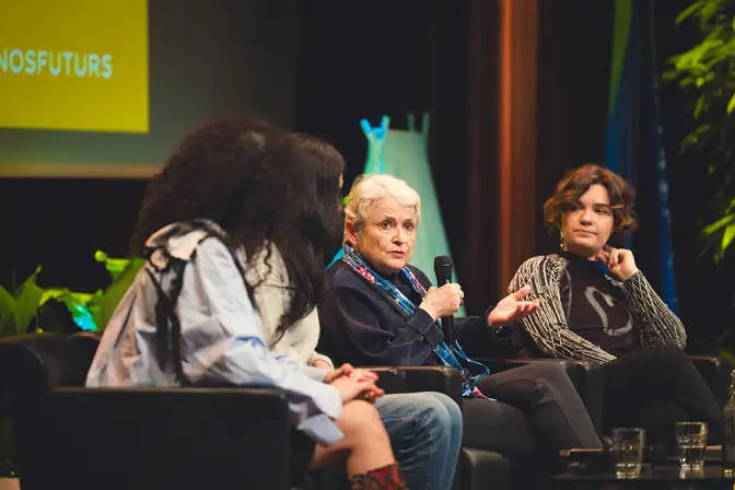 Cette photo nous montre quatre femmes, deux de dos et deux de face, en train de parler d'un sujet à l'occasion de l'événement Nos Futurs 2024. Ces femmes sont assises dans des canapés sur une scène.