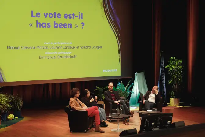 Une photographie de la scène de l'auditorium des Champs Libres, durant une rencontre du festival Nos Futurs 2024. Quatre personnes se tiennent sur la scène, assises dans des fauteuils.