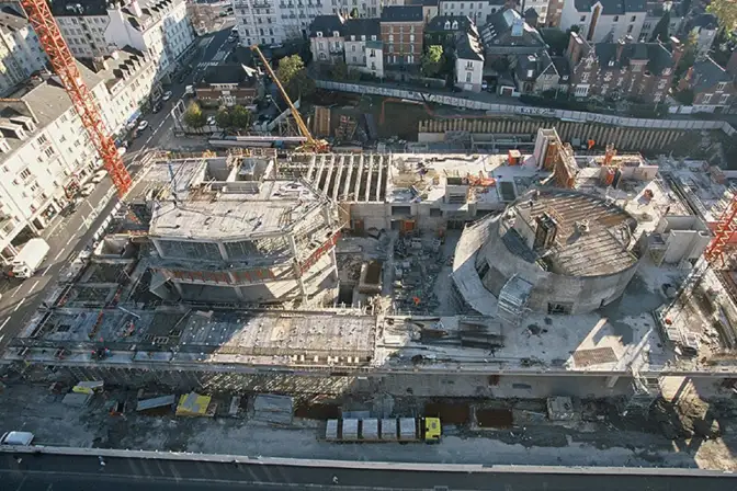 Photo d'une vue en contre-plongée depuis la place Charles de Gaulle de la construction du bâtiment des Champs Libres : on distingue déjà la tour de la Bibliothèque et le dôme de l'Espace des sciences.