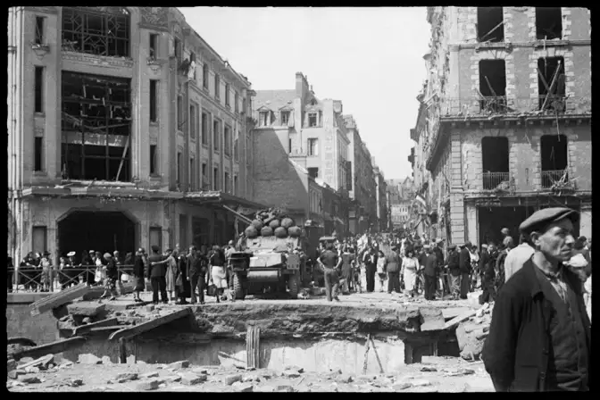 Vue d'immeubles endommagés par les bombardements. La foule est dans la rue autour d'un trou béant dans la rue.