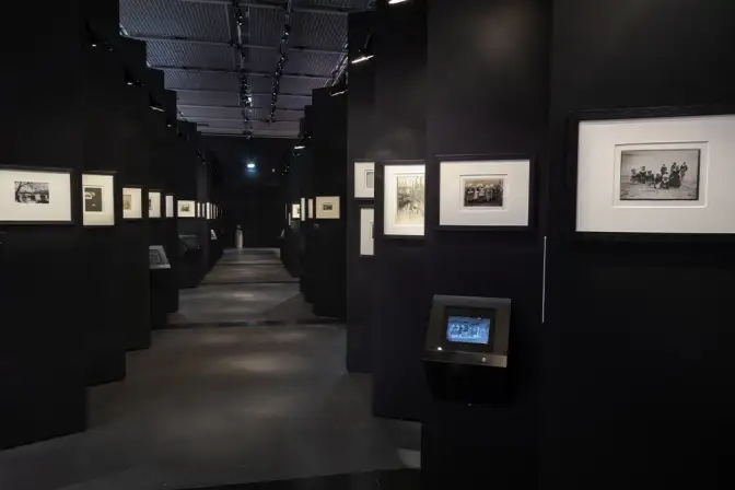 Vue d'un couloir sombre, mobilier d'exposition noir, sur lequel sont alignés beaucoup de murs d'expositions portant des photos des frères.