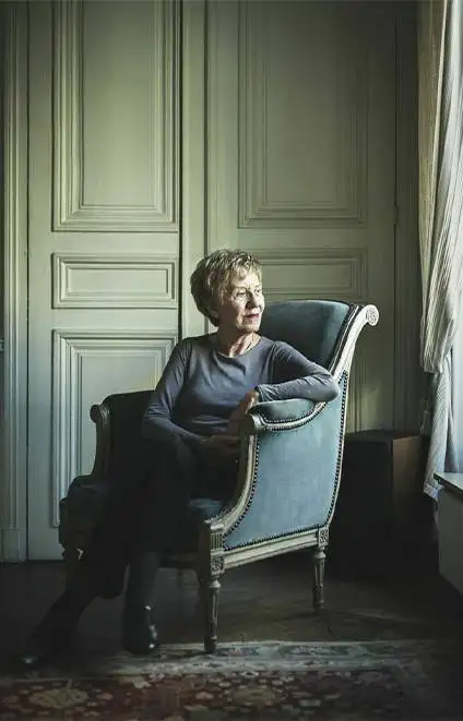 Une photographie de Michelle Perrot, assise dans un fauteuil élégant. Elle regarde dehors par la fenêtre.