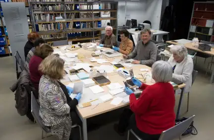 une dizaine de personnes autour d'une table du centre de documentation travaille au reconditionnement des plaques photographiques