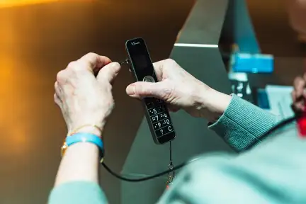 Une femme âgée tient dans ses mains un appareil d'audioguide, elle s'apprête à le brancher à son casque audio.