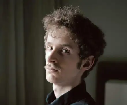 Une photographie du visage de Jérôme Blin qui regarde l'objectif dans un décor de chambre.