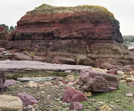 Photographie de l'Ande de Bréhec en Côtes d'armor. Une roche rouge se détache d'une plage de galet.