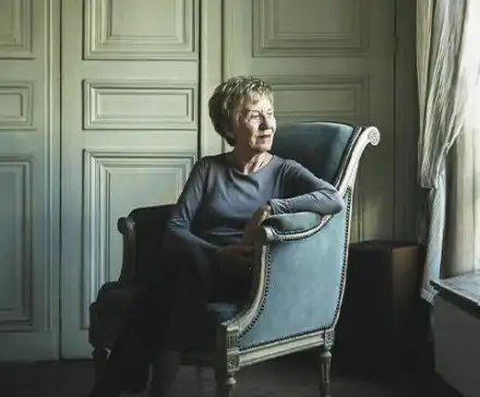 Une photographie de Michelle Perrot, assise dans un fauteuil élégant. Elle regarde dehors par la fenêtre.