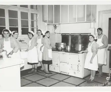 Photographie en noir et blanc d'un groupe de femmes en tablier dans une cuisine