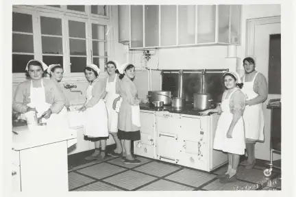 Photographie en noir et blanc d'un groupe de femmes en tablier dans une cuisine