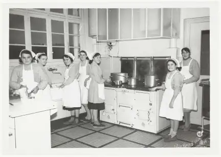 Photographie en noir et blanc d'un groupe de femmes en tablier dans une cuisine