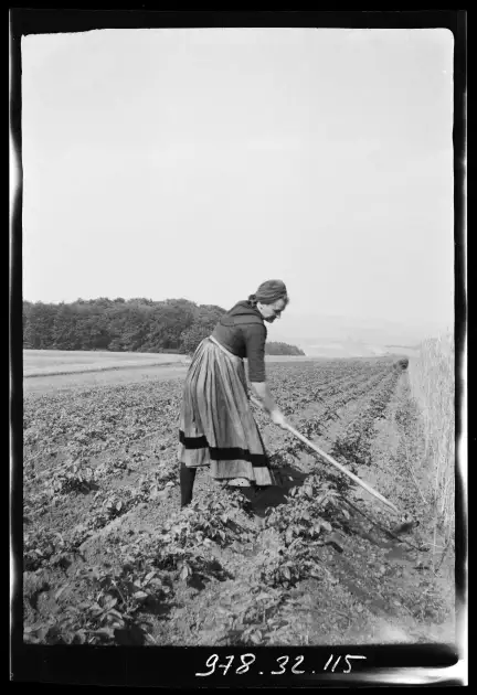 Photographie en noir et blanc d'une femme travaillant avec un outil dans un champ.